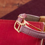 Close-up of a Cartier Tortue pink leather watch strap with a gold buckle, resting on a red textured book.