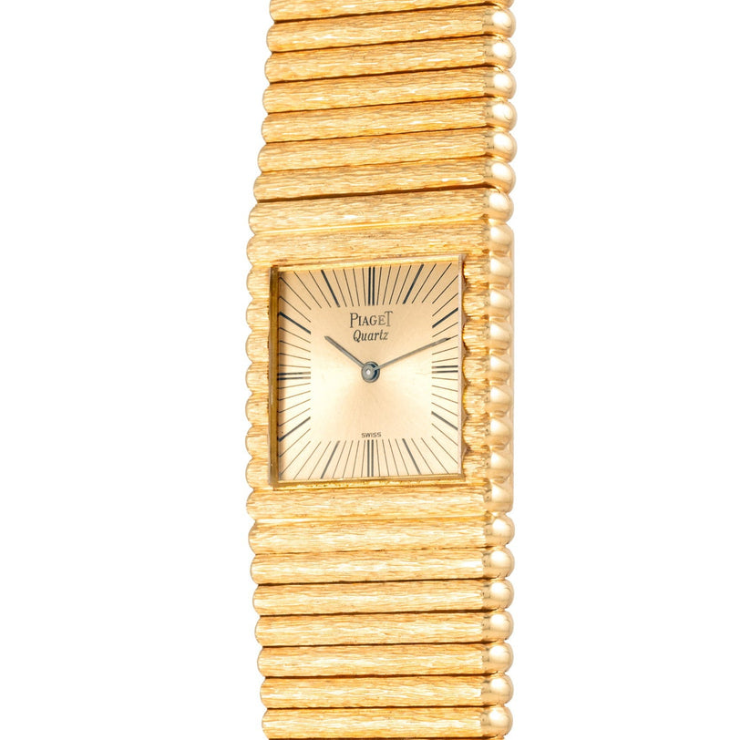The Piaget Emperador is a gold quartz wristwatch featuring a textured band and rectangular face with black hour markers.