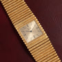 A Piaget Emperador gold Quartz wristwatch with a textured band, displayed on a dark red leather surface.