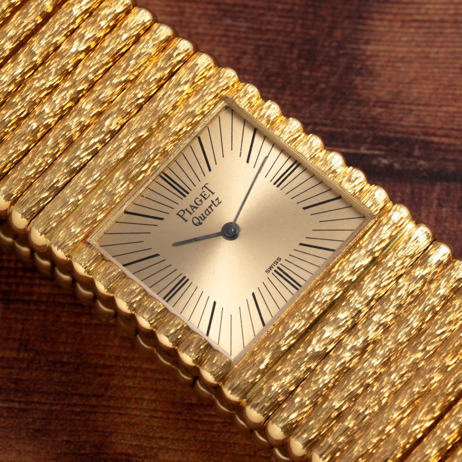 The Piaget Emperador quartz watch with a textured bracelet rests on a wooden surface.