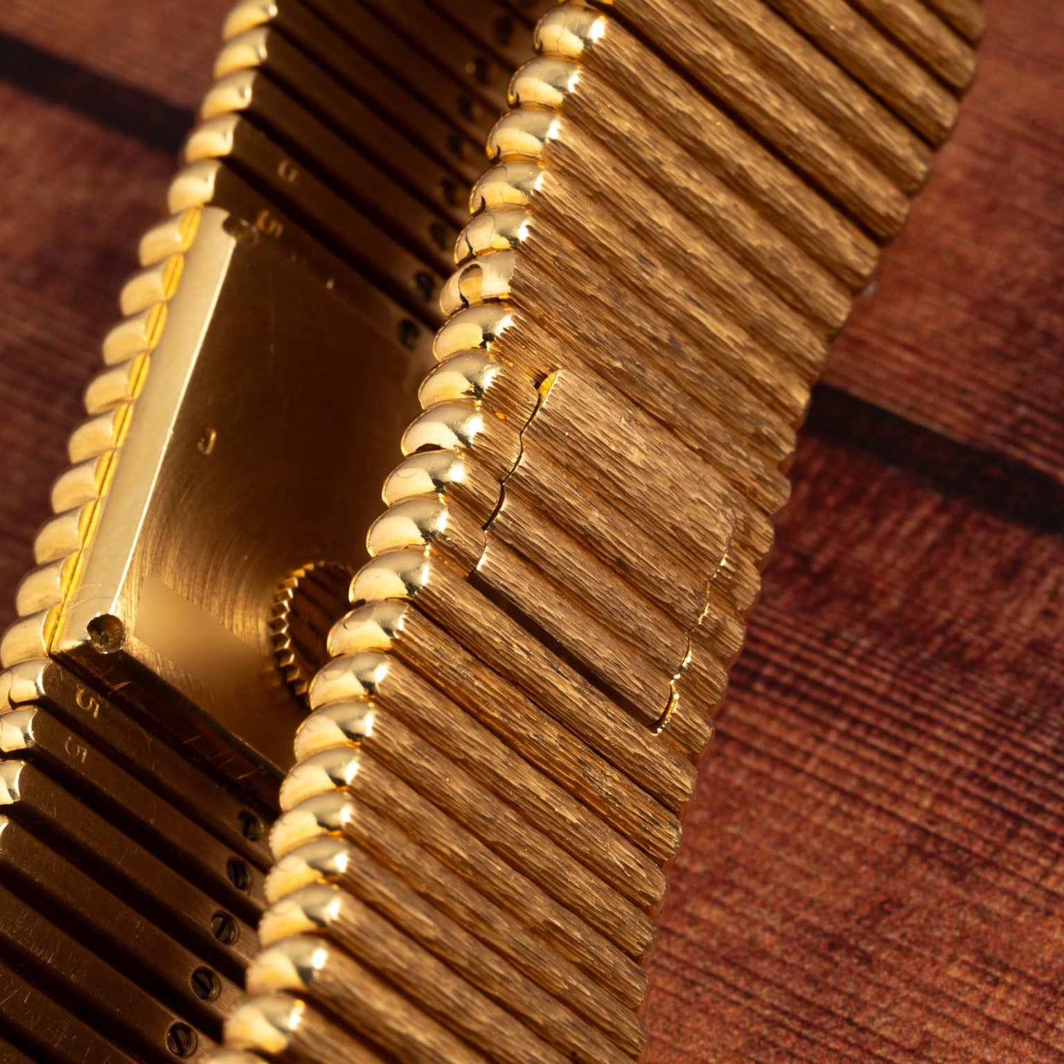 Close-up of the Piaget Emperador gold-toned metal watch band, featuring a textured, wood-like pattern, displayed on a wooden surface.