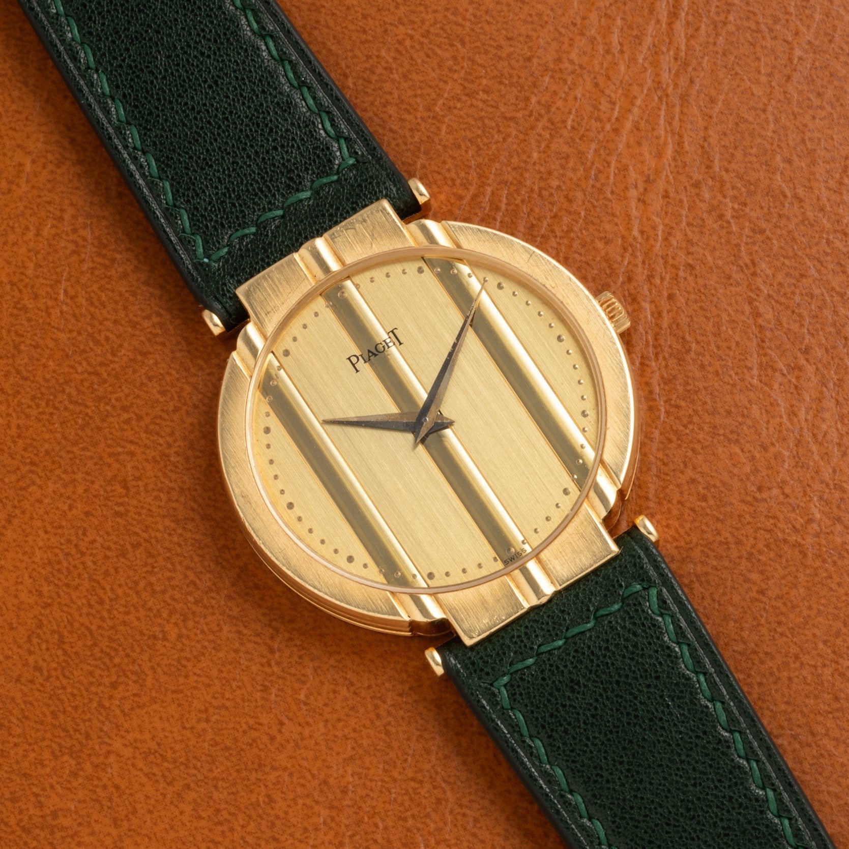 Piaget Polo Large gold wristwatch with a green leather strap, displayed on a brown leather background.