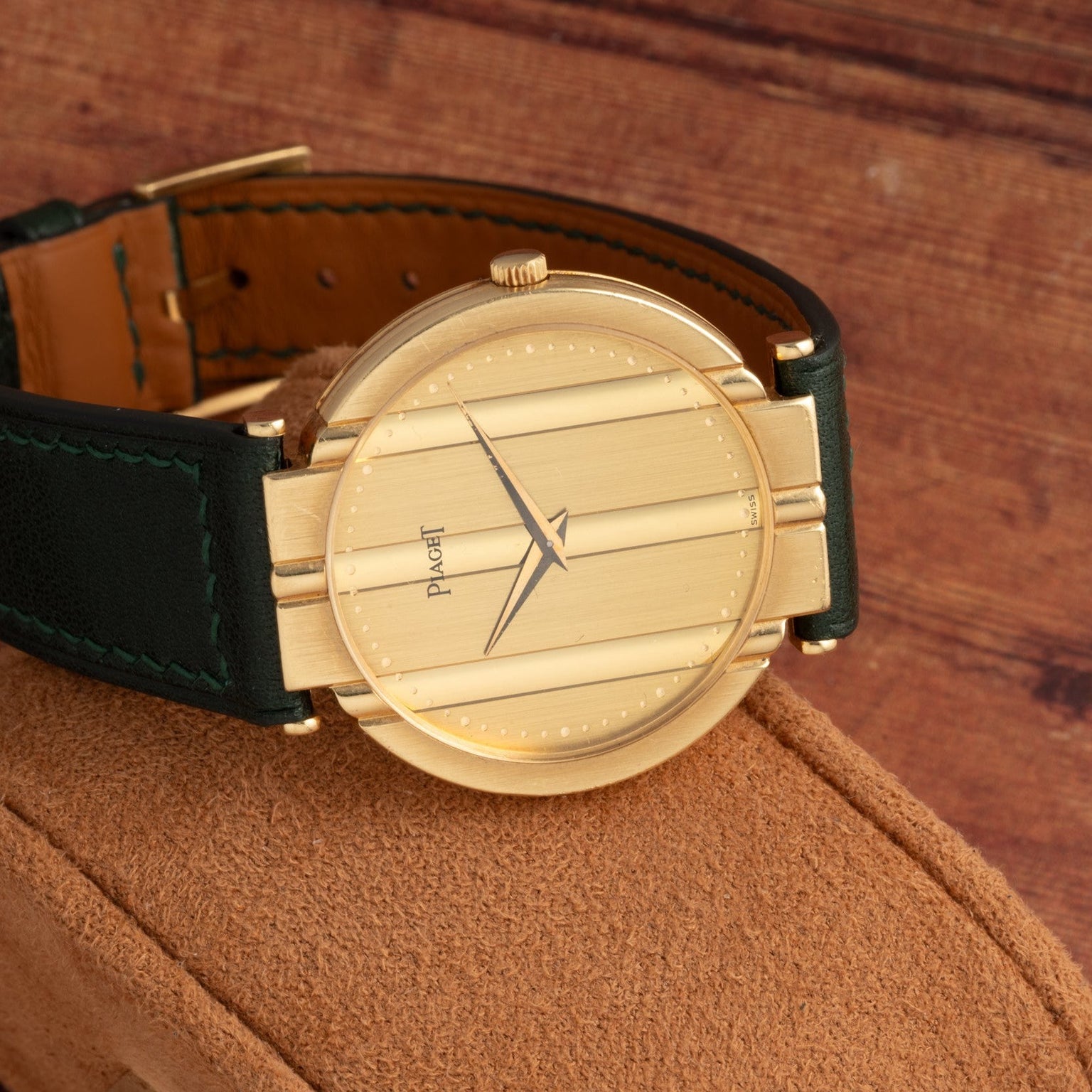 A Piaget Polo Large gold wristwatch with a black leather strap rests on a tan suede surface.