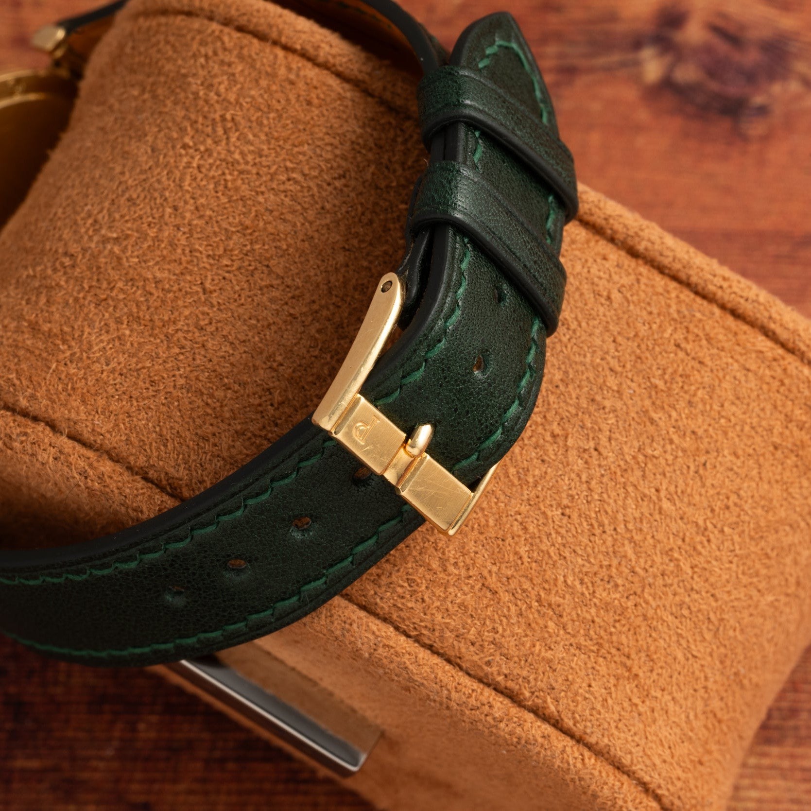 Close-up of the Polo Large by Piaget, featuring a green leather strap with a gold buckle, displayed on a brown suede watch box.