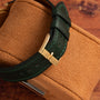 Close-up of the Polo Large by Piaget, featuring a green leather strap with a gold buckle, displayed on a brown suede watch box.
