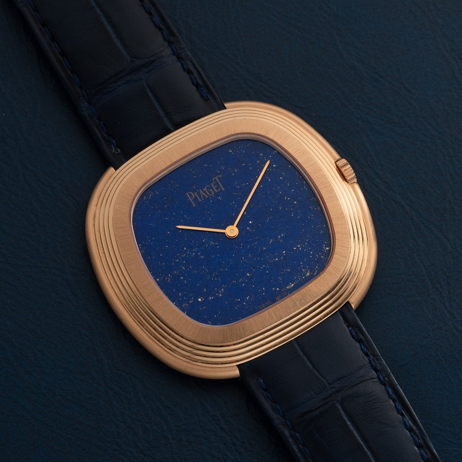 A Piaget Black Tie Andy Warhol wristwatch with a blue speckled dial and black leather strap is displayed on a dark surface.