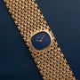 The Patek Philippe Ellipse Ladies Woven Cuff wristwatch, featuring a blue oval face, is displayed on a dark blue textured surface.