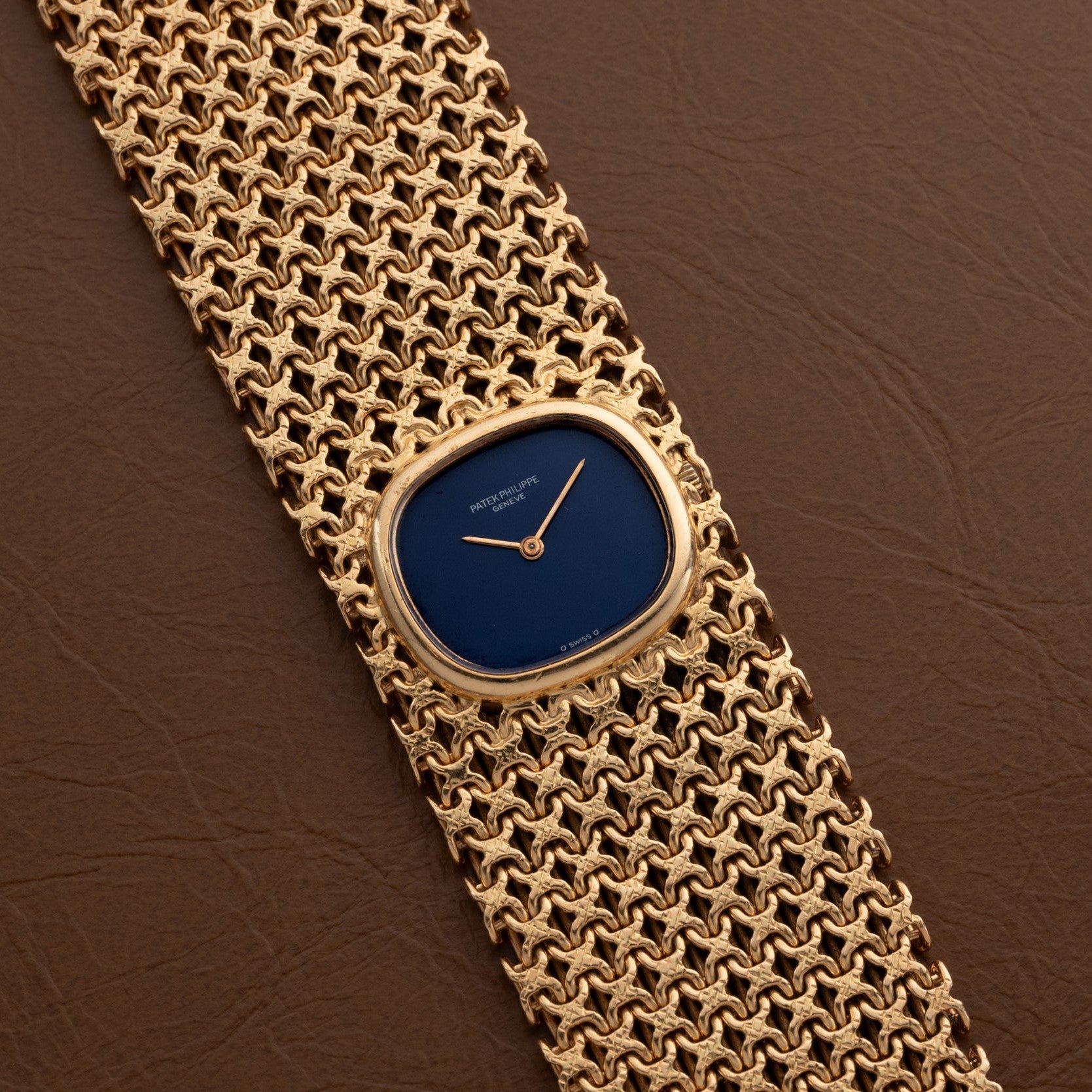 Patek Philippe Ellipse Ladies Woven Cuff: a gold wristwatch with a blue face and textured gold mesh band displayed on brown leather.