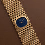 Patek Philippe Ellipse Ladies Woven Cuff: a gold wristwatch with a blue face and textured gold mesh band displayed on brown leather.