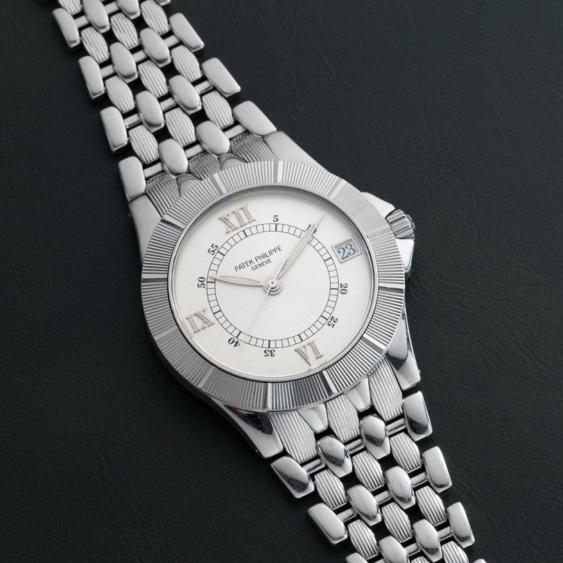 A Patek Philippe Neptune silver wristwatch featuring a date window rests on a dark textured surface.