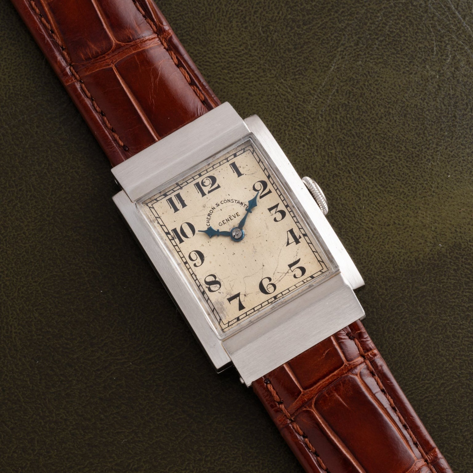 A Vacheron Constantin Rectangular Steel Dress Watch with a brown leather strap displayed on a textured dark green surface.