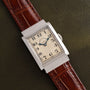 A Vacheron Constantin Rectangular Steel Dress Watch with a brown leather strap displayed on a textured dark green surface.