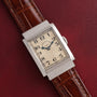 A Vacheron Constantin Rectangular Steel Dress Watch with a brown leather strap displayed on a textured burgundy surface.