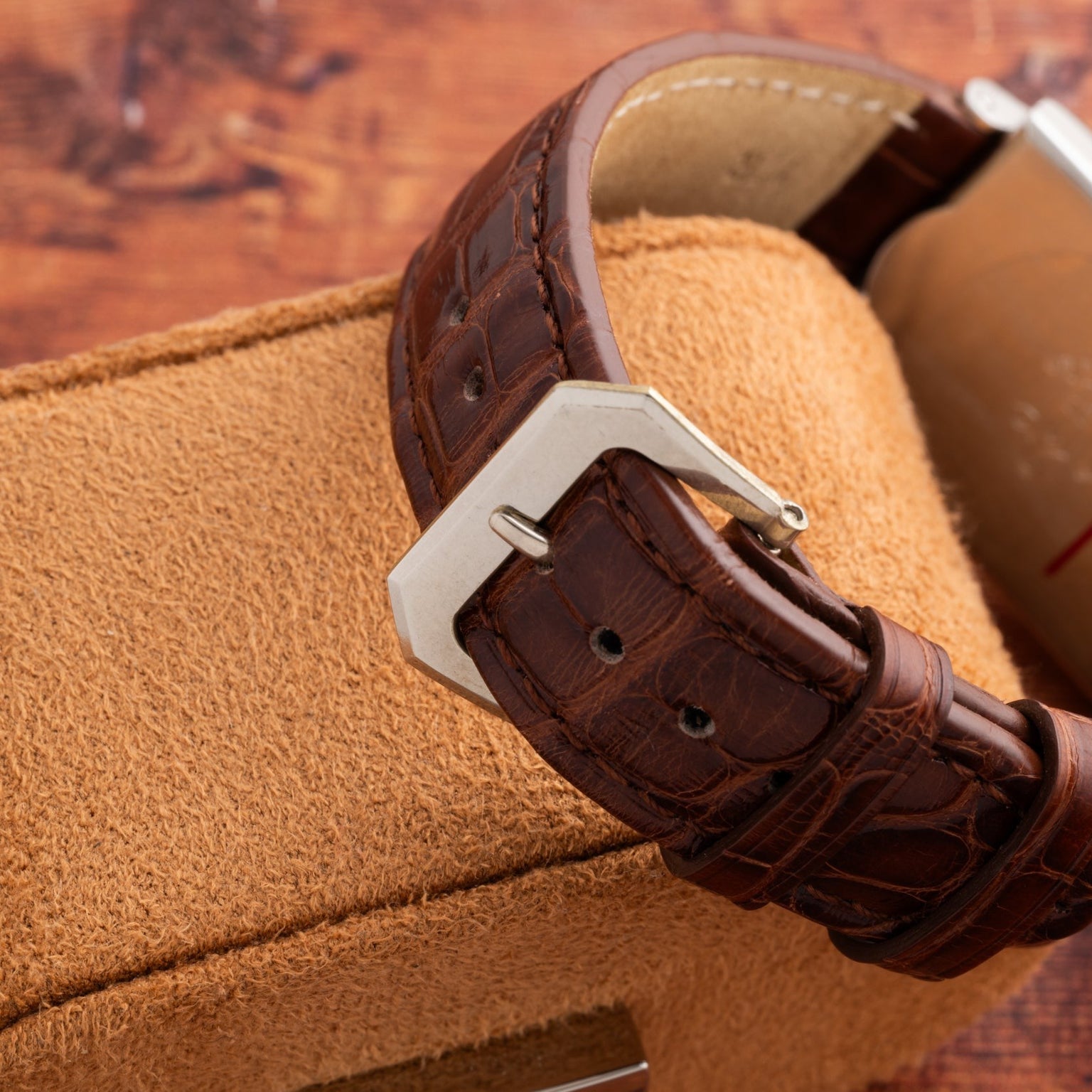 Close-up of the Vacheron Constantin Rectangular Steel Dress Watch’s brown leather strap and silver buckle, displayed on a tan cushion.