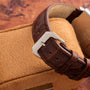 Close-up of the Vacheron Constantin Rectangular Steel Dress Watch’s brown leather strap and silver buckle, displayed on a tan cushion.
