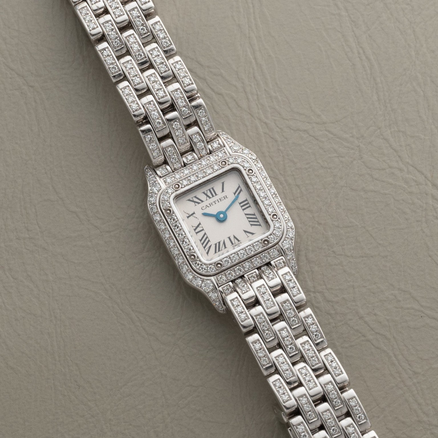 Panthère Diamond by Cartier, a silver wristwatch with a square diamond-set bezel and bracelet, displayed on a textured beige surface.