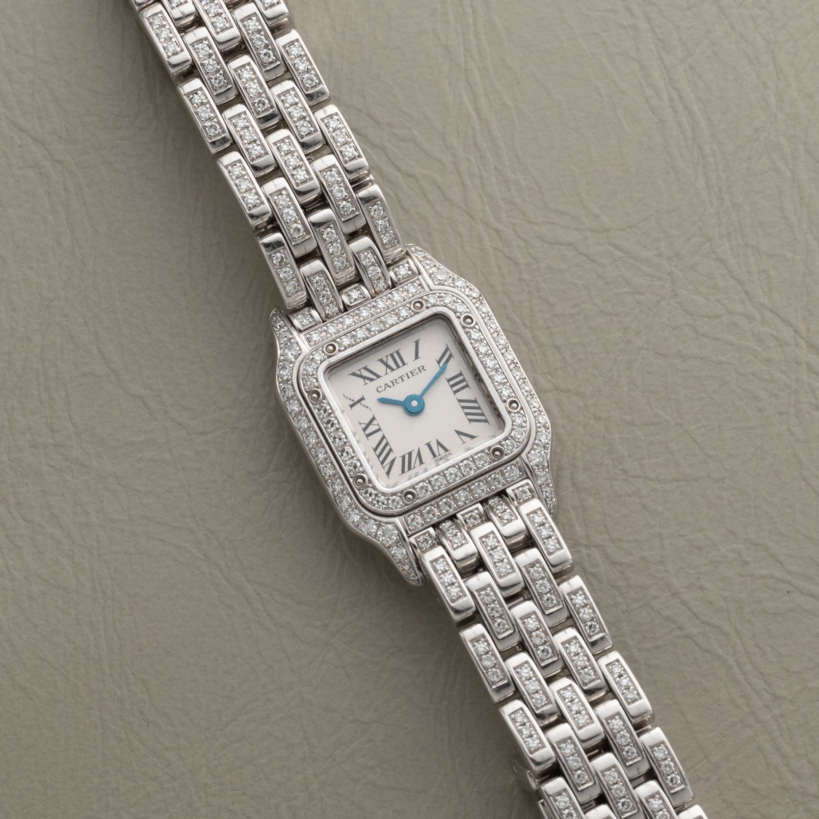 Panthère Diamond by Cartier, a silver wristwatch with a square diamond-set bezel and bracelet, displayed on a textured beige surface.