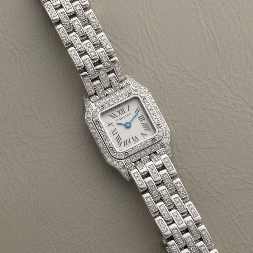 Panthère Diamond by Cartier, a silver wristwatch with a square diamond-set bezel and bracelet, displayed on a textured beige surface.