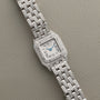 Panthère Diamond by Cartier, a silver wristwatch with a square diamond-set bezel and bracelet, displayed on a textured beige surface.