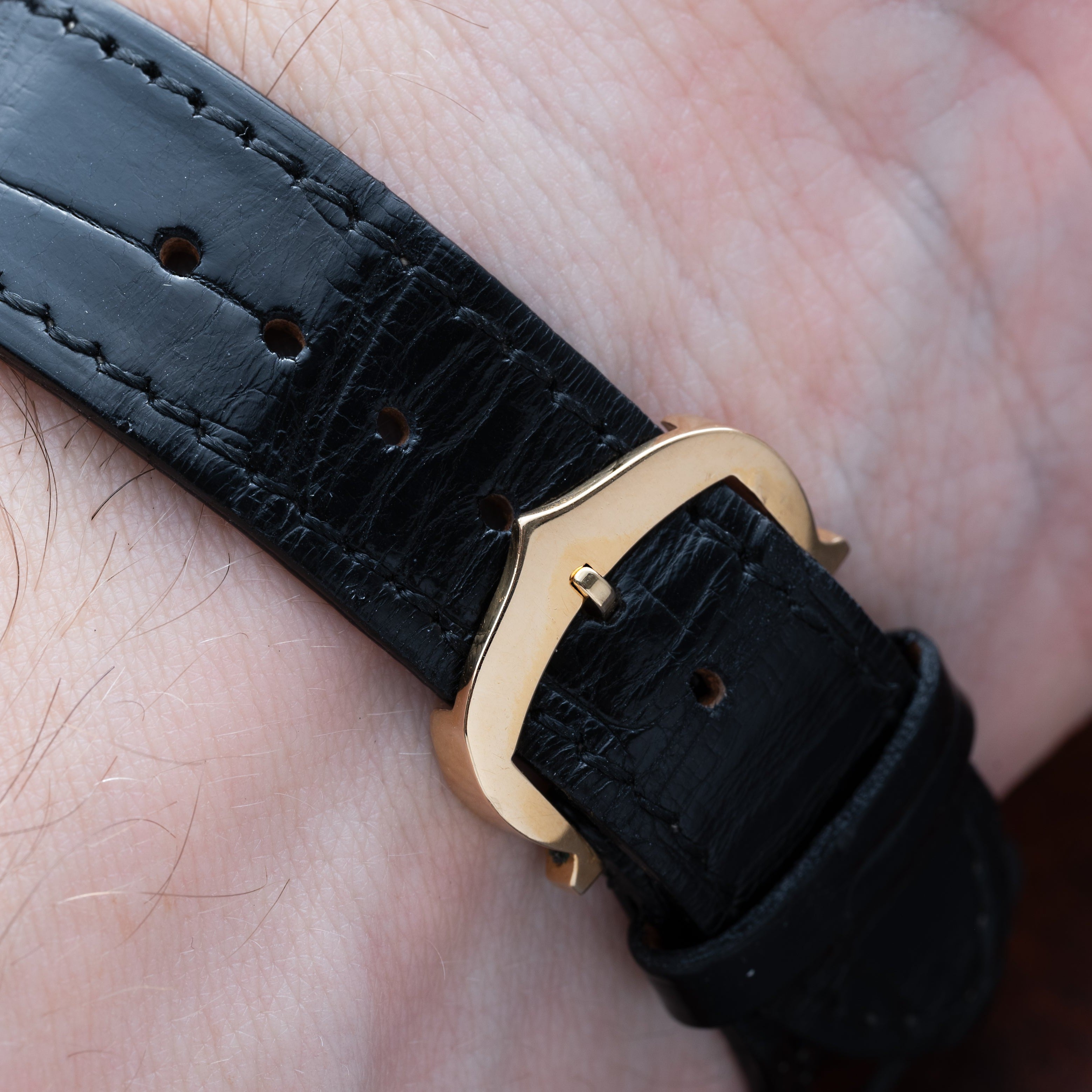 Close-up of the Cartier Tank Louis watch featuring a black leather strap with a gold buckle on a persons wrist.