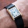 A Cartier Tank Louis wristwatch with a black leather strap on a persons wrist.