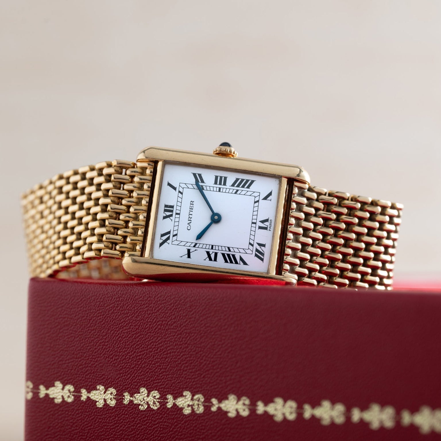 Cartier Tank Louis gold watch featuring a white Roman numeral dial, displayed on a red decorative box.