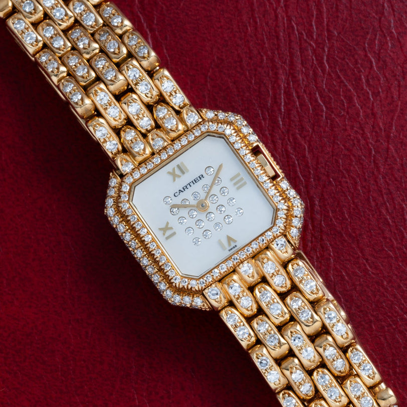 The Cartier Ceinture Paris Diamond watch, featuring diamond accents, is displayed on a red leather background.
