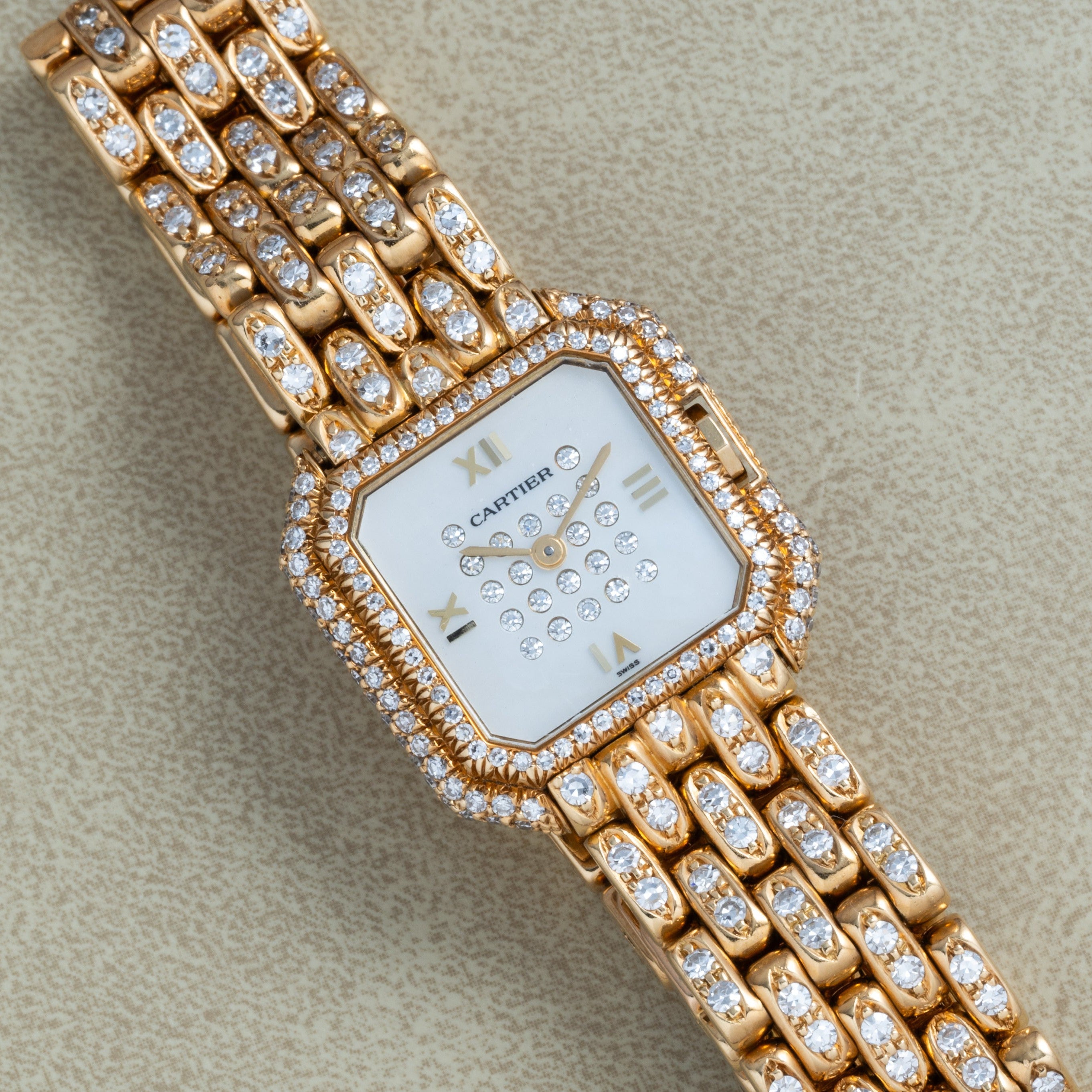 The Cartier Ceinture Paris Diamond watch features a gold case, diamond bezel and bracelet, and Roman numerals on a white face.