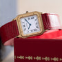 Cartier Santos Dumont gold watch featuring Roman numerals and a red leather strap, displayed on a red box.