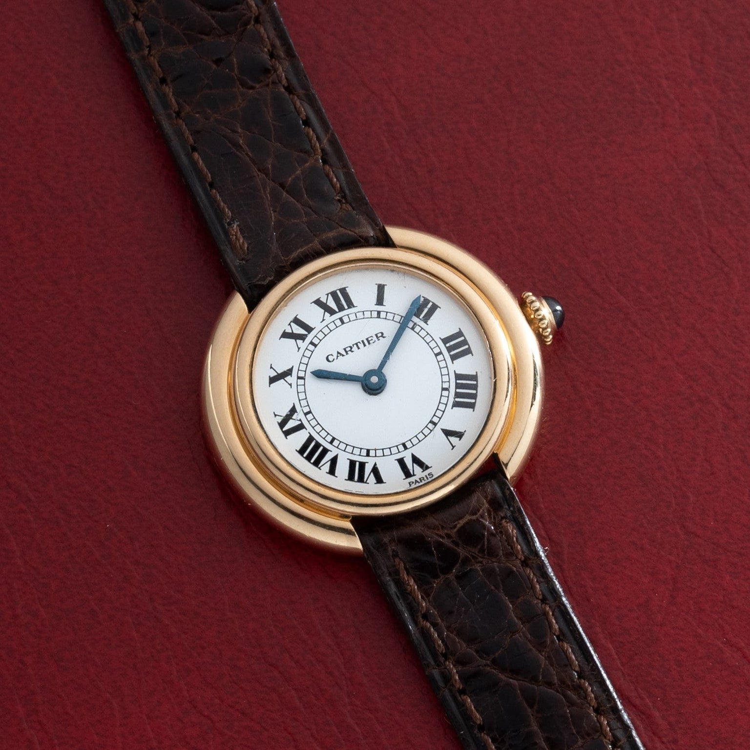 A Cartier Vendome gold wristwatch with a brown leather strap displayed on a red textured background.