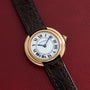 A Cartier Vendome gold wristwatch with a brown leather strap displayed on a red textured background.