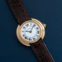 A Cartier Vendome watch with a brown leather strap and Roman numeral dial, displayed on a dark blue surface.
