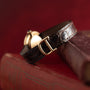 The Cartier Vendome brown leather watch with a gold buckle is displayed atop old books against a dark red background.