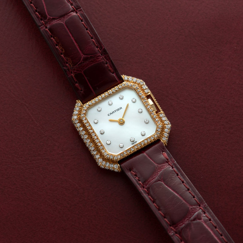 The Cartier Ceinture Diamond watch features diamond accents and a burgundy leather strap, showcased on a matching burgundy surface.