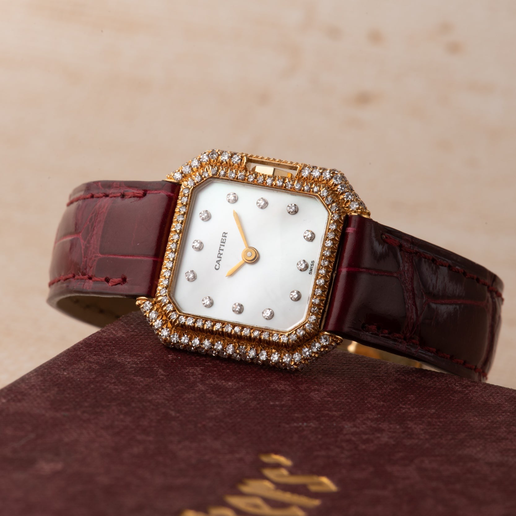 The Cartier Ceinture Diamond watch features a diamond-studded design with a maroon leather strap, displayed on a matching Cartier box.
