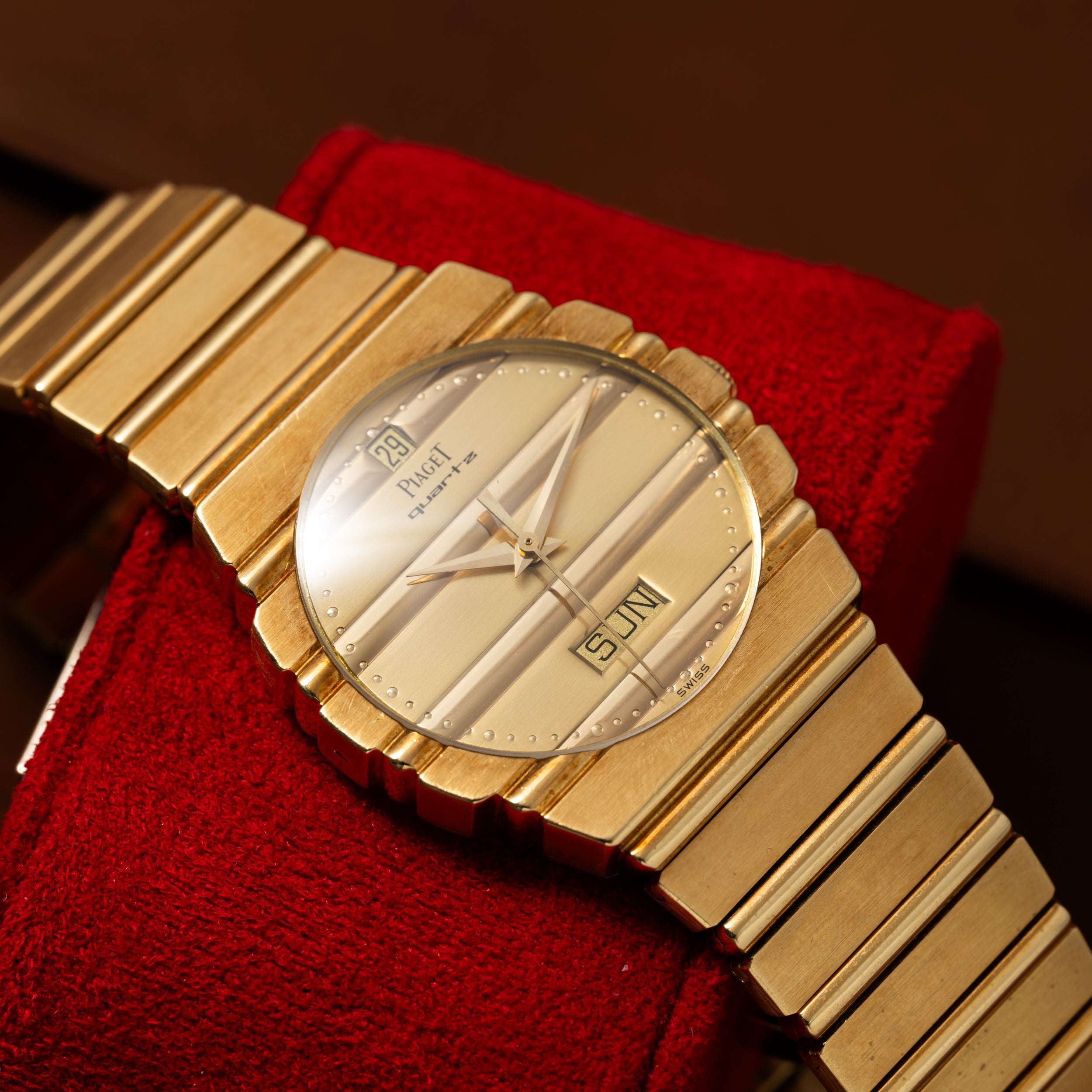 Piaget Polo Calendar wristwatch with day and date display, resting on a red fabric cushion.