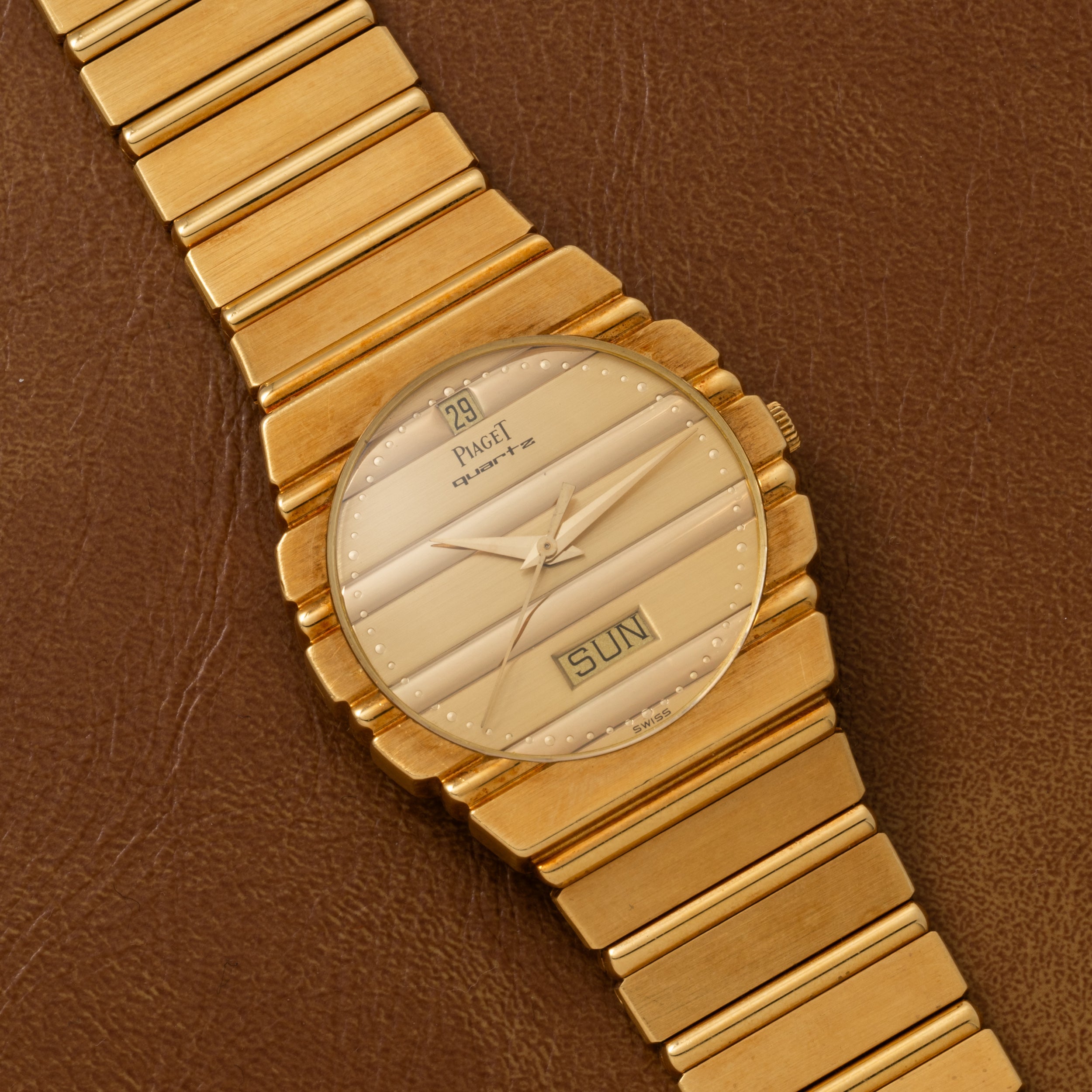 The Piaget Polo Calendar gold wristwatch features a textured dial with date and day display, shown on a brown leather surface.