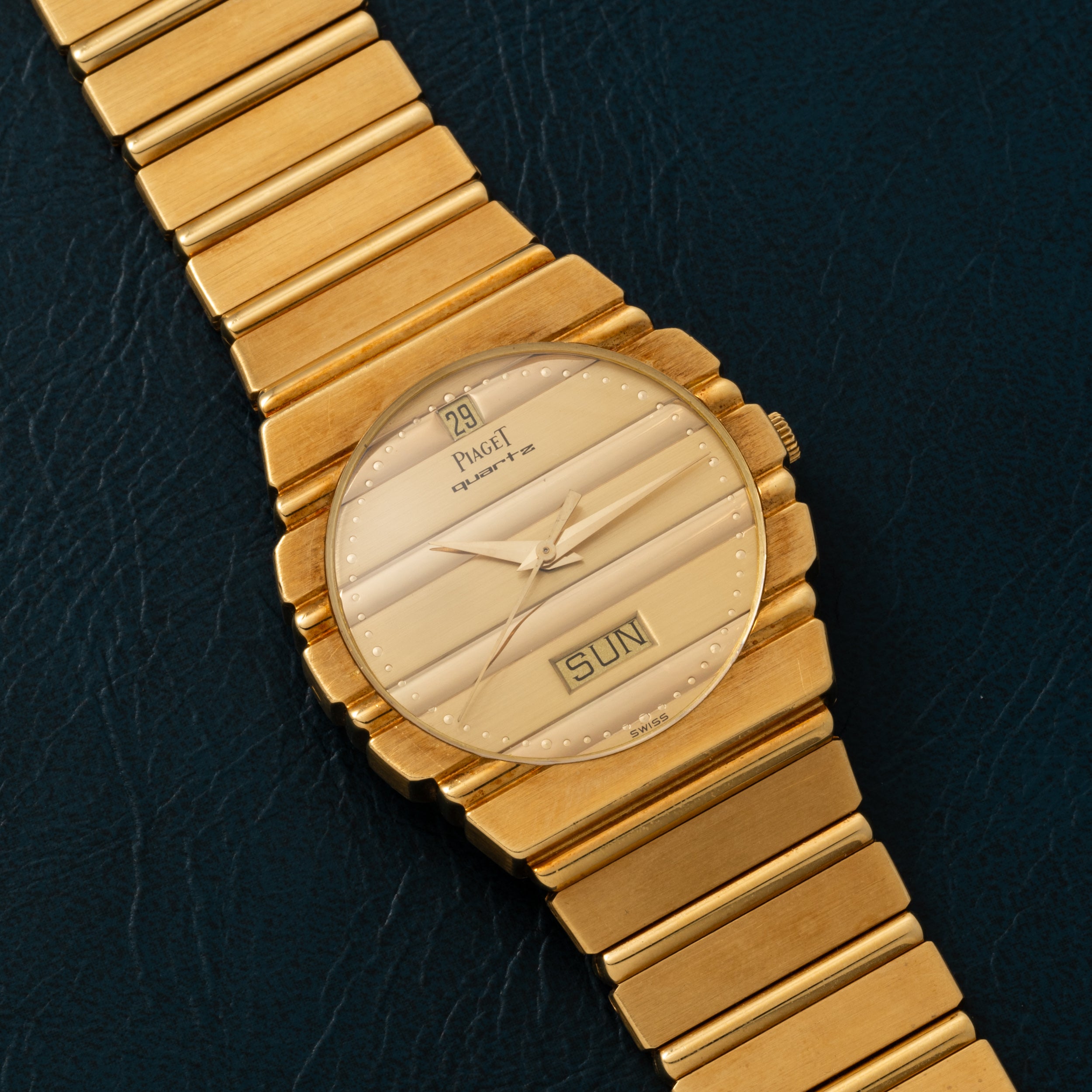 Piaget Polo Calendar wristwatch featuring a gold case and a striped dial with date and day display on a dark textured background.