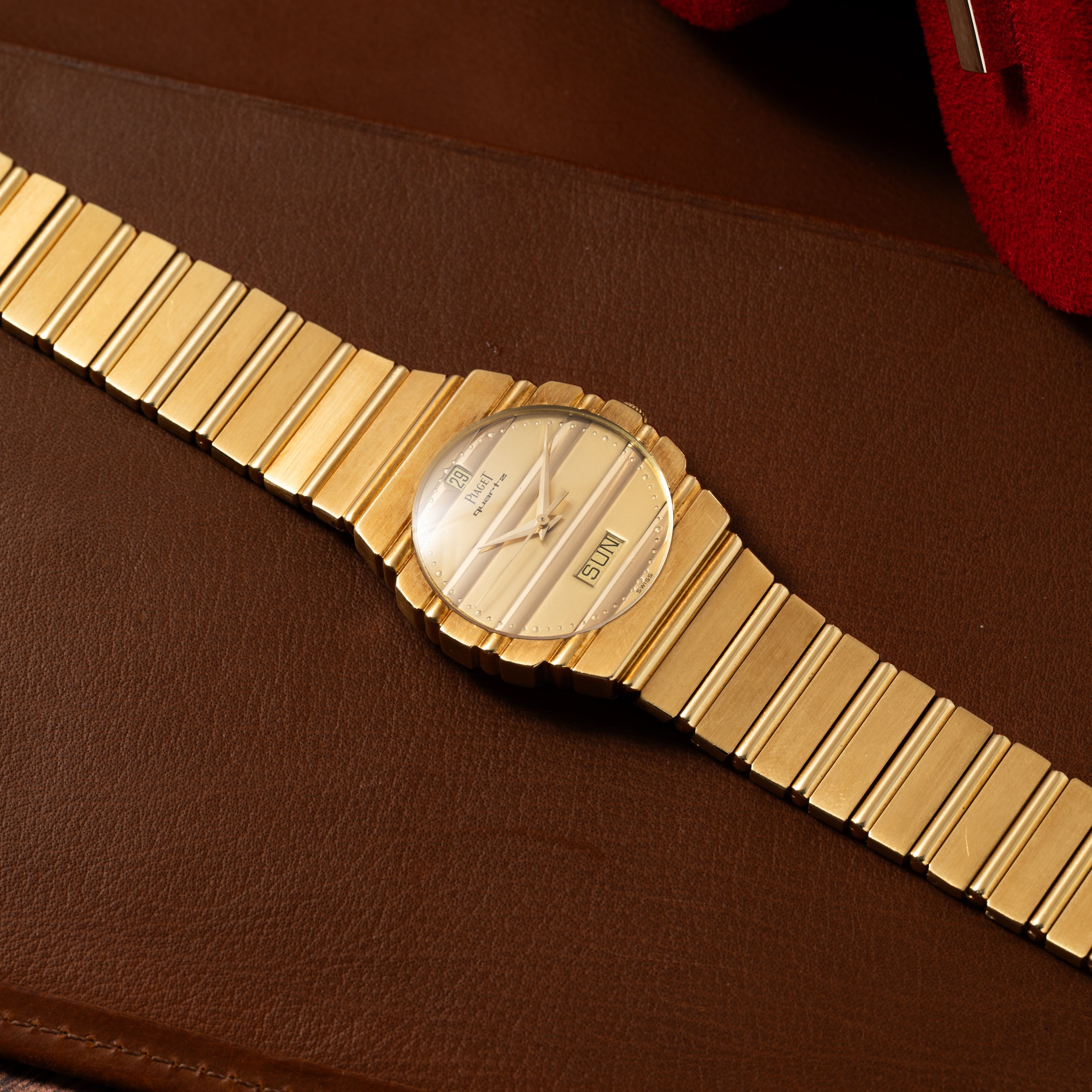 A Piaget Polo Calendar watch with a metal band displayed on a brown leather surface.