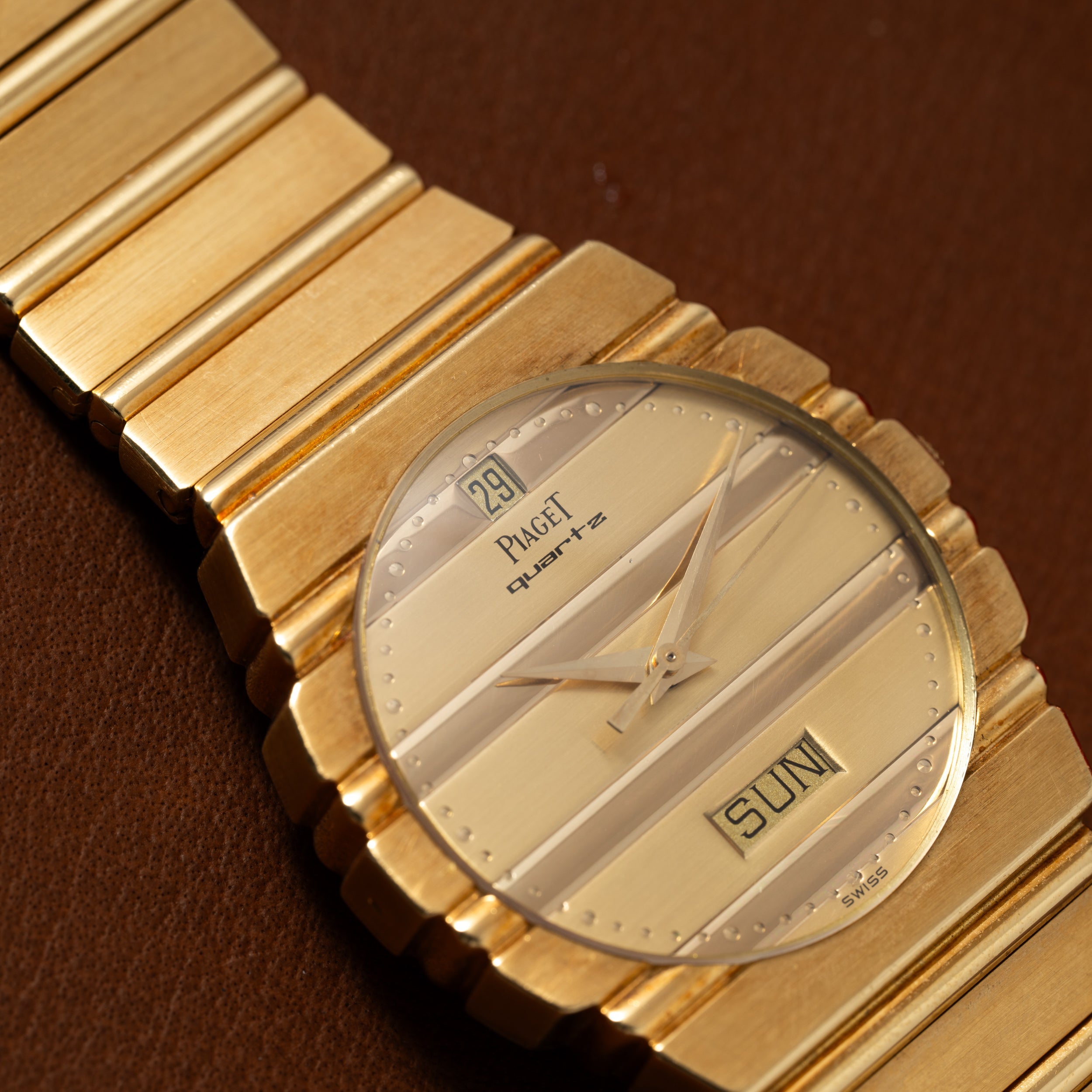 Close-up of a Piaget Polo Calendar watch displaying day and date, resting on a brown surface.