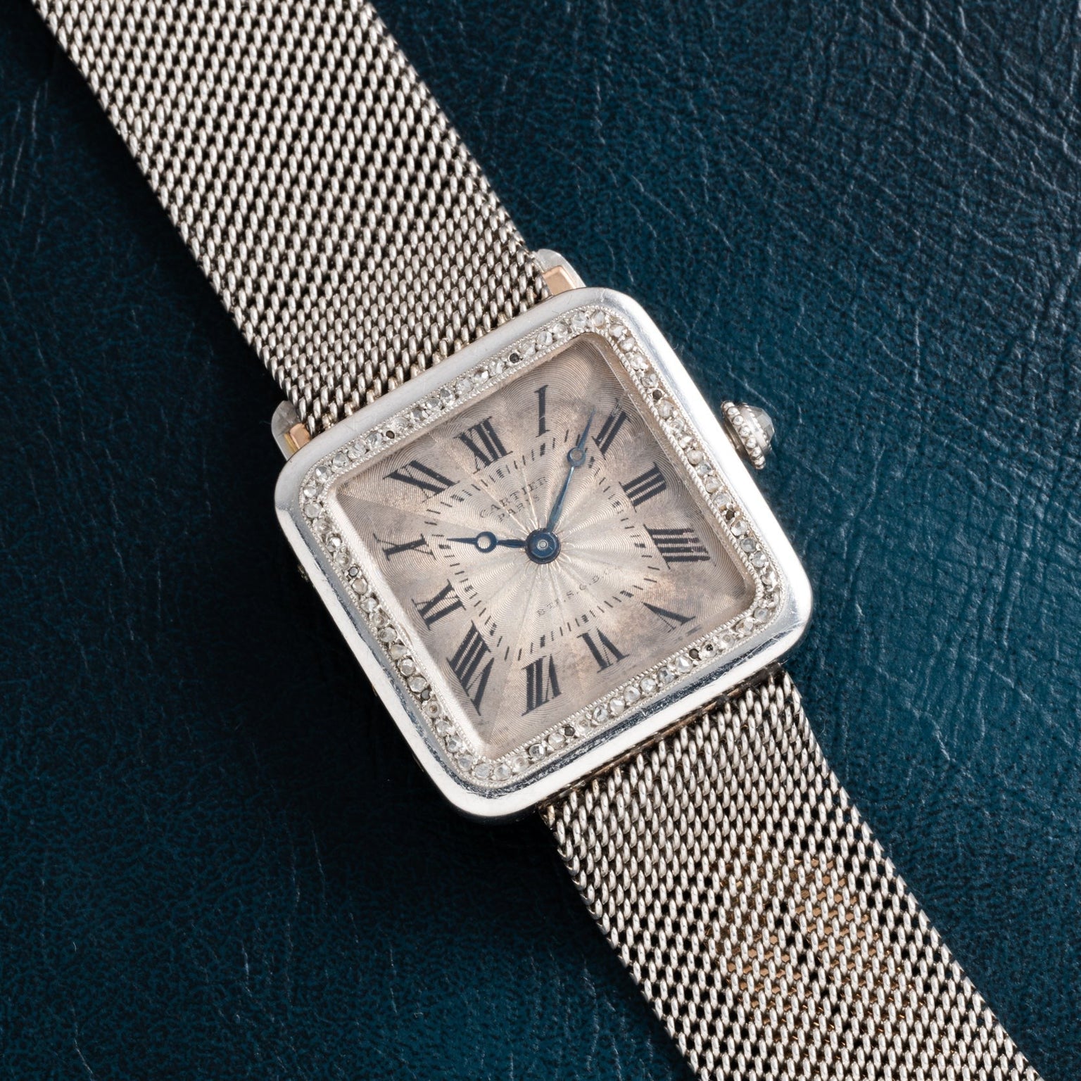 The Cartier Santos Platinum features a square platinum face, diamond bezel, and mesh band, shown against a dark textured background.