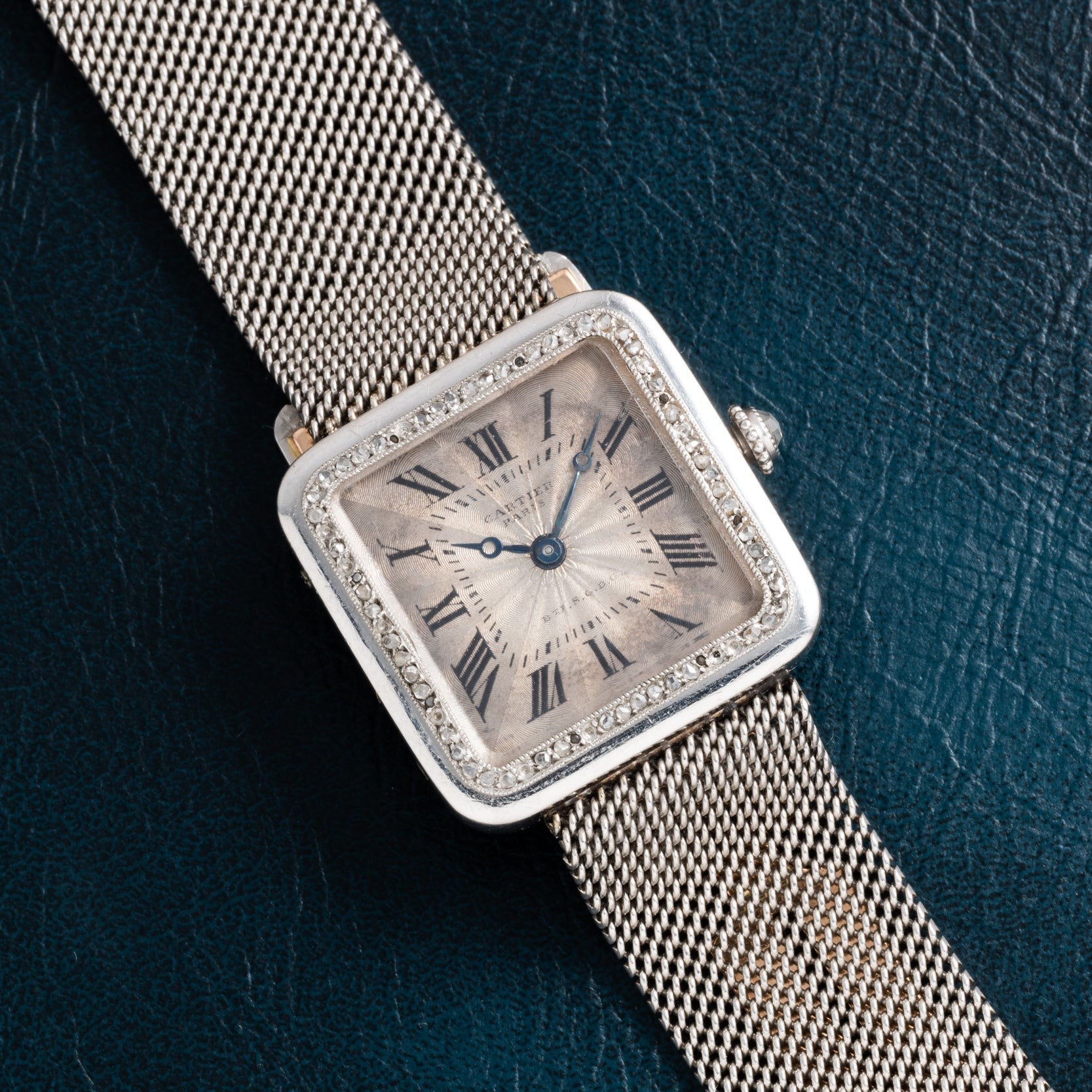 The Cartier Santos Platinum features a square platinum face, diamond bezel, and mesh band, shown against a dark textured background.