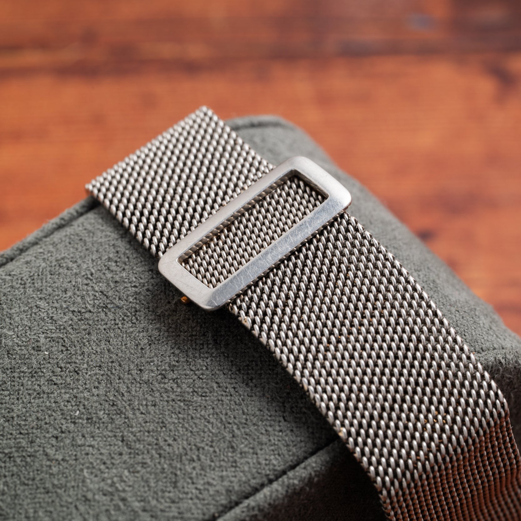 A close-up of the Cartier Santos Platinum’s silver mesh strap on a green textured surface, set against a blurred brown background.