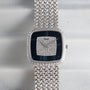 The Piaget Hawk Eye White Gold Dress Watch features a textured band and a diamond-studded square face, displayed on a light surface.