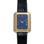 A Piaget Tank Blue Lapis rectangular gold wristwatch with a blue face, Roman numerals, and a black leather strap.