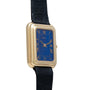 The Piaget Tank Blue Lapis is a gold rectangular wristwatch featuring a blue face, Roman numerals, and a black leather strap.