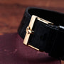 Close-up of the gold buckle on the Piaget Tank Blue Lapis black leather strap, resting on a maroon textured surface.