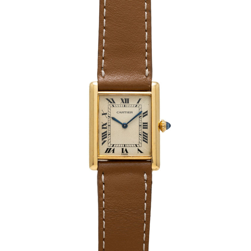 The Cartier Tank Louis is a gold watch featuring a square face, Roman numerals, and a brown leather strap with white stitching.