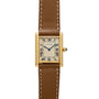 The Cartier Tank Louis is a gold watch featuring a square face, Roman numerals, and a brown leather strap with white stitching.