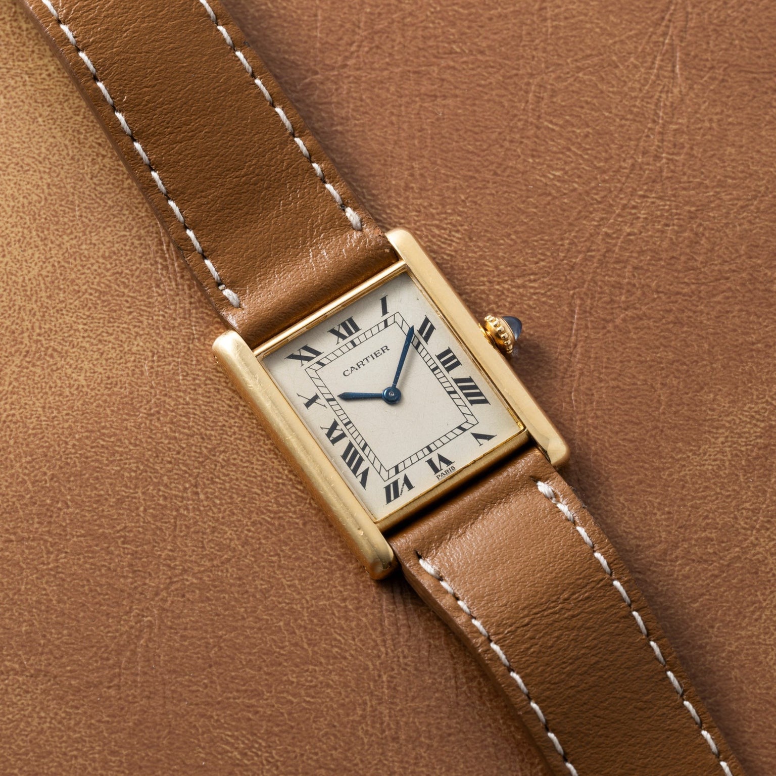 A Cartier Tank Louis watch with a brown leather strap rests on a matching brown leather surface.